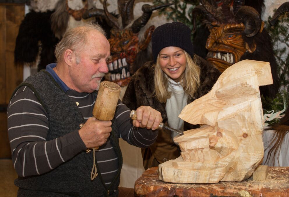 Ein Mann der eine traditionelle Perchtenmaske aus Holz schnitzt.