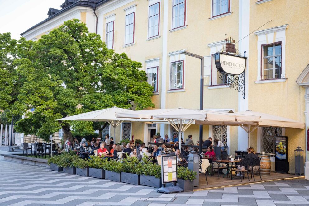 Gemütliche Terrasse des Restaurants Benediktus im Schloss Mondsee mit Sitzplätzen im Freien und Blick auf die Basilika Mondsee