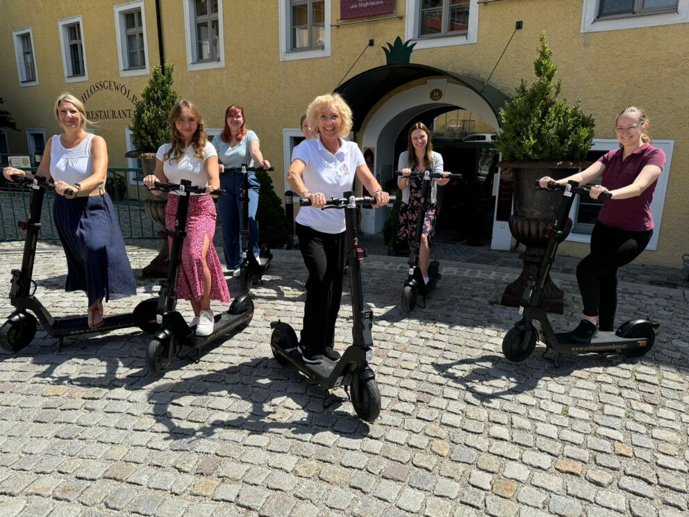 Unser Team mit modernen E-Scootern vor dem Schlosshotel Mondsee – nachhaltige Mobilität für Gäste und Ausflüge in der Region